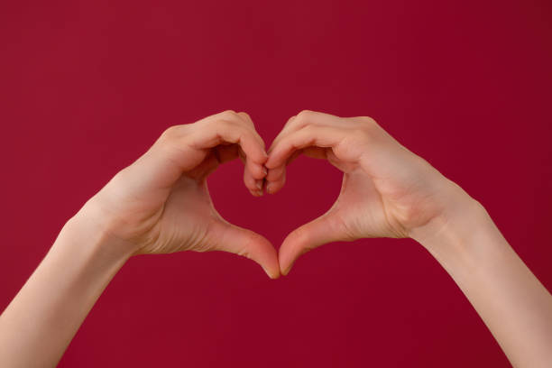istock Female hands showing heart sign on red background in studio 1298424306