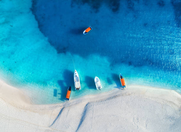 Aerial view of the yachts and fishing boats on tropical sea coast with white sandy beach at sunset in summer. Zanzibar, Africa. Colorful landscape with boats, transparent blue water. Top view. Travel stock photo