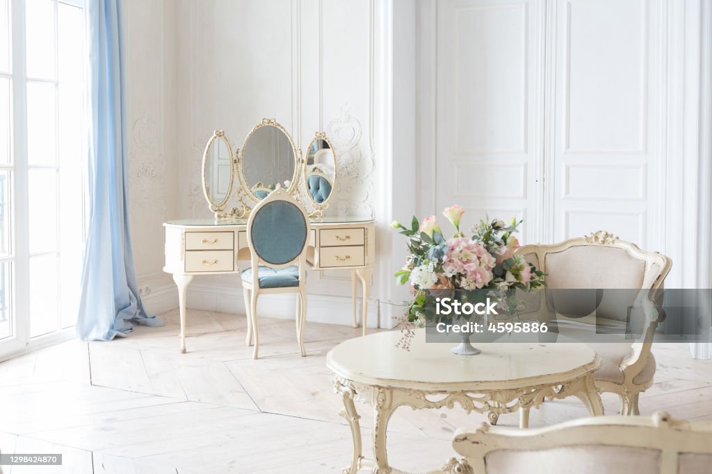luxurious light interior in the Baroque style. A spacious room with a road chic beautiful furniture, a fireplace and flowers. plant stucco on the walls and light wood parquet Apartment Stock Photo