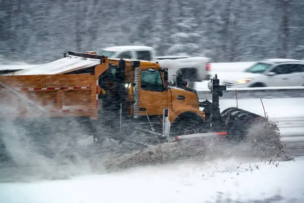 A snowplow clears heavy snow from a multi-lane highway.