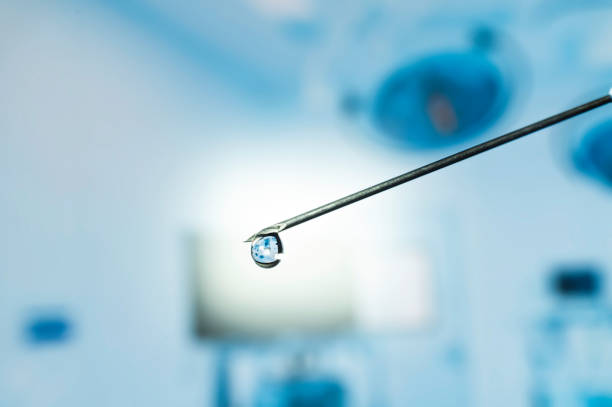 Syringe needle with a drop of serum on top. Blurred background that is reflected in the serum drop.