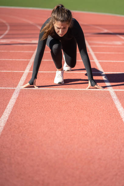 istock woman sprinter on a treadmill rubber stadium or running track getting ready to start run. 1298428967