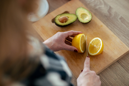 Close-up of mature woman's hands while she cutting lemon over wooden table in the kitchen at home.