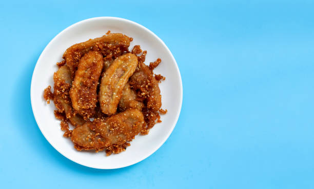istock Fried bananas on white dish plate on blue background. Thai snack 1298432029
