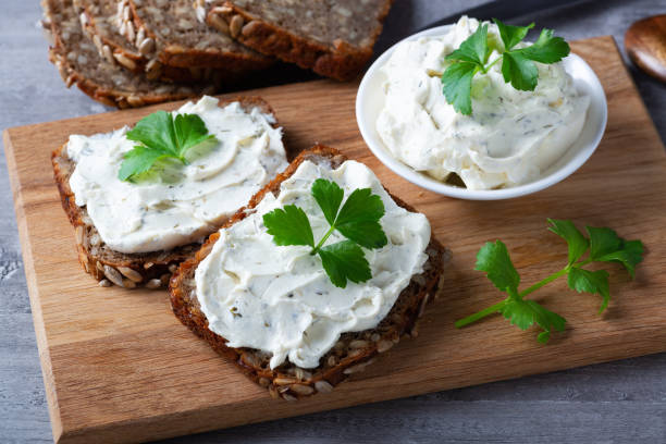 istock Home made bread on a wooden cutting board with curd cheese and ricotta and herbs. Decorated with green herbs 1298436621