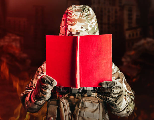Soldier in uniform and armor helmet holding opened red book.