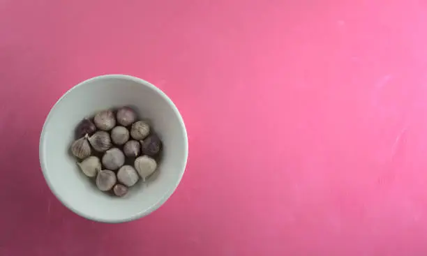 Photo of Garlic in bowl on acrylic scratchy pink canvas background. Food, kitchen, eating, still life photography with copy space.