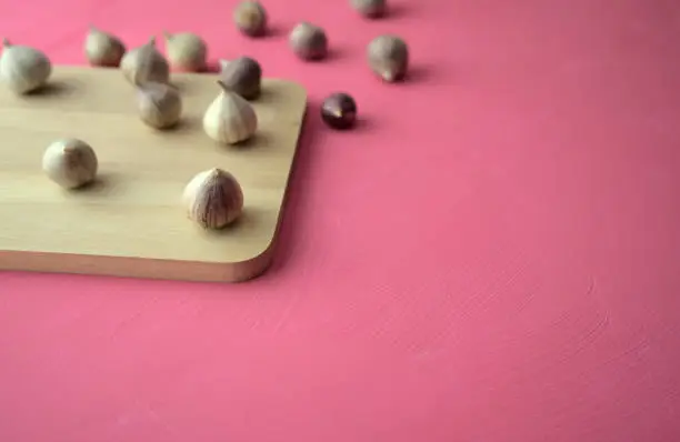 Photo of Garlic on cutting board on acrylic scratchy pink canvas background. Food, kitchen, eating photography with copy space.