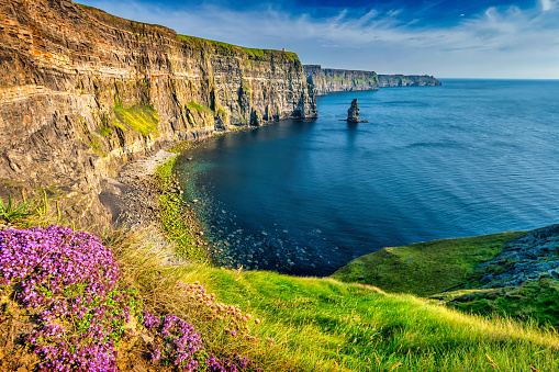 Landscape with dark misty cliffs and waves splashing over rocks and sun shining through - Ireland