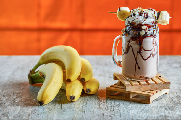 koktajl mleczny bananowy ze śmietaną, czekoladą i gałęzią bananów na marmurowym tle - smoothie banana smoothie milk shake banana zdjęcia i obrazy z banku zdjęć