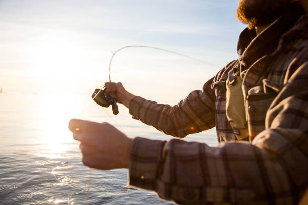um close-up de um pescador de moscas vestindo uma camisa xadrez, segurando uma vara e carretel - fishing rod fishing fishing reel casting - fotografias e filmes do acervo