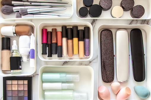 Top view of female visagiste is neatly placing cosmetic and vanity items in MUJI's PP makeup storage boxes with various sizes on white marble dressing table. Decluttering and organization concept.