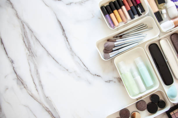 Uporządkowany makijaż i pędzle w białych pojemnikach na marmurowym blacie, ilustrujące schludną toaletkę.