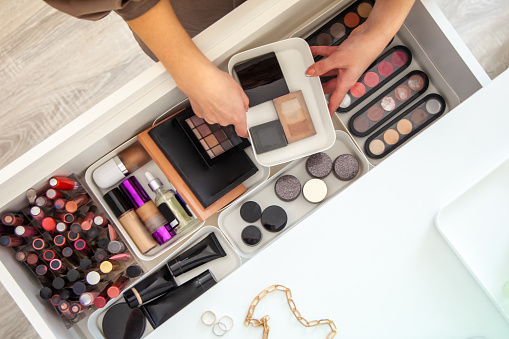Woman hands neatly organizing makeup or cosmetics in the drawer of vanity dressing table and leaving her jewellery on dressing table surface. Visagiste is taking out vanity case of cosmetic powders