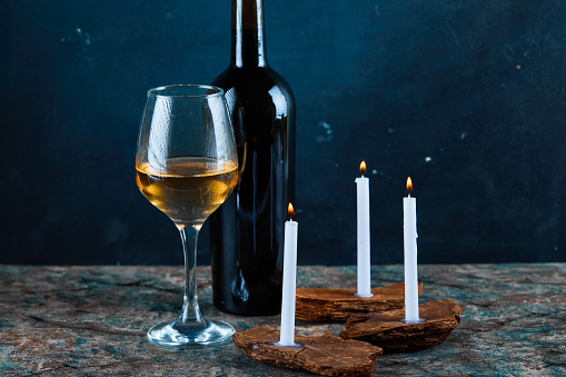 A glass of white wine and bottle on marble table with candles. High quality photo