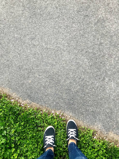 Looking down at two feet standing in grass before crossing into the road/pathway.