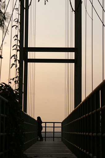 A large metal structure is silhouetted against a sunset sky with a woman looking out at the view