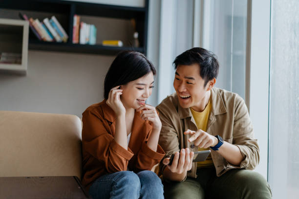 Happy and smiling Asian Chinese couple watching a show on smartphone together Image of Asian Chinese man and woman watching a show on smartphone together in living room chinese couple stock pictures, royalty-free photos & images
