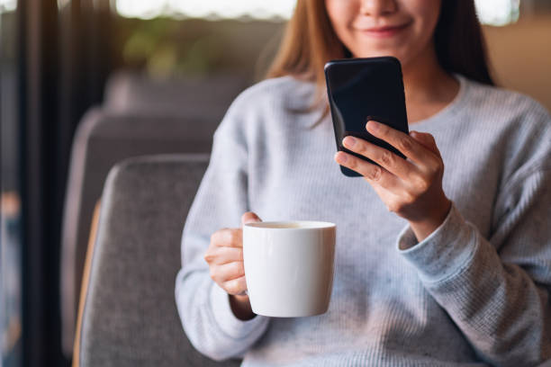 istock a beautiful young asian woman holding and using mobile phone while drinking coffee 1298491482