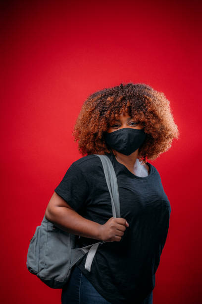 istock Young African American Woman Smiling Under a Cloth Protective Face Mask Wearing a Backpack Getting Ready for School in COVID-19 1298494176