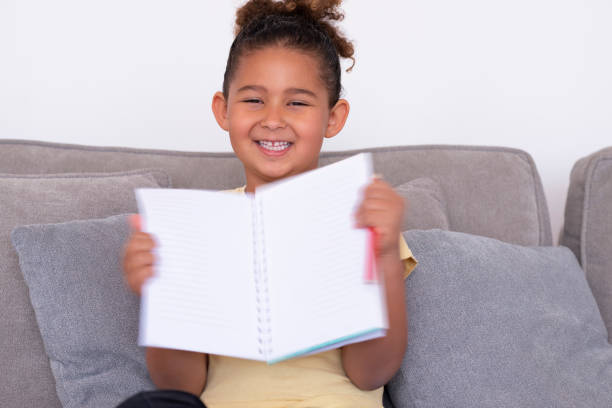 istock Happy schoolgirl opening, showing blank notepad. 1298494227