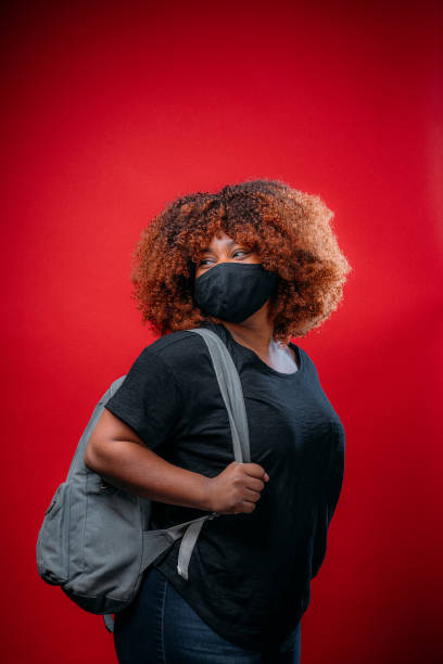 istock Young African American Woman Smiling Under a Cloth Protective Face Mask Wearing a Backpack Getting Ready for School in COVID-19 1298494442