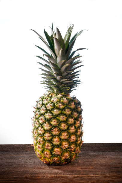 istock Big pineapple with its leaves on a barn wood board on white background 1298495463