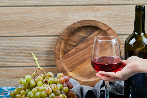 Bunch of grapes, a glass of red wine and a bottle of wine on wooden background. High quality photo