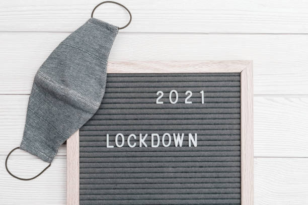 istock Grey colored Flatlay letter board with message text lockdown 2021 and protective face mask. Lock down loading concept. 1298503629