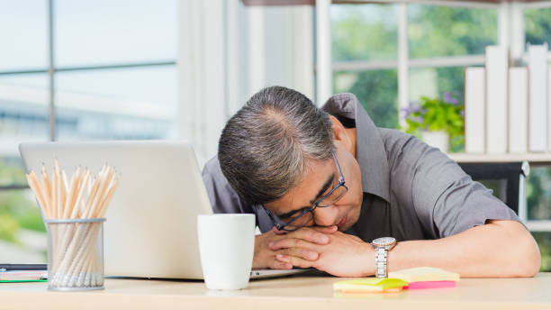 businessman tired overworked he sleeping over a laptop computer Asian businessman tired overworked he sleeping over a laptop computer on the desk. senior man with eyeglasses lying asleep on table at his working place narcolepsy stock pictures, royalty-free photos & images