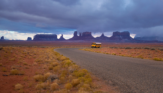 Yellow school bus driving early in the morning on Monument valley