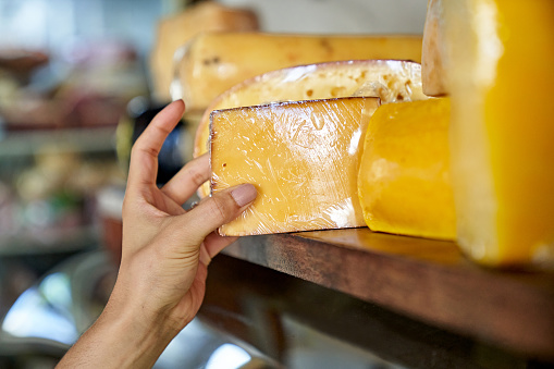 Close-up of young woman choosing from a selection of cheeses displayed in gourmet grocery store.