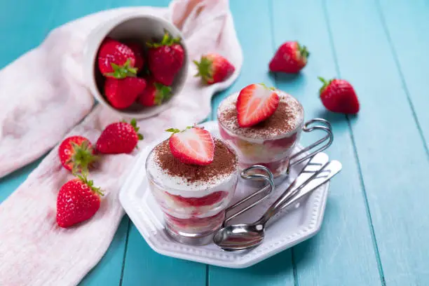 Strawberry tiramisu - traditional italian dessert in a glass on a light blue background.