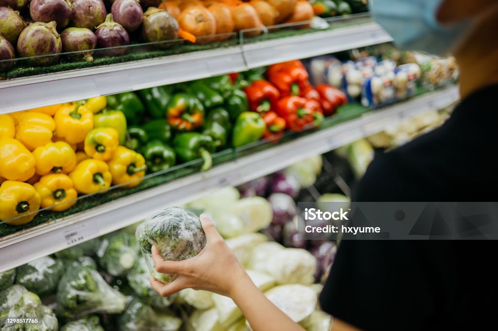 Asian woman with protective face mask shopping for fresh vegetables in supermarket Image of an Asian woman wearing protective face mask and shopping for fresh vegetables in supermarket during Covid-19 pandemic. Groceries Stock Photo