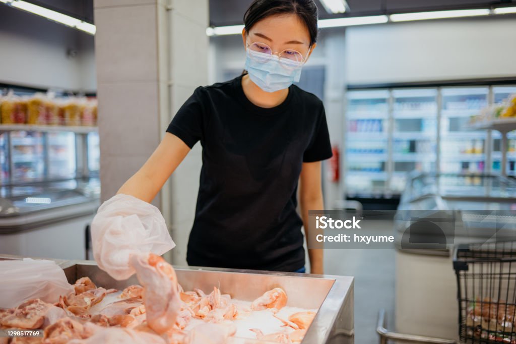 An Asian Chinese woman with protective face mask buying fresh chicken meat in supermarket Image of an Asian Chinese woman with protective face mask choosing fresh chicken meat in supermarket Chicken Meat Stock Photo