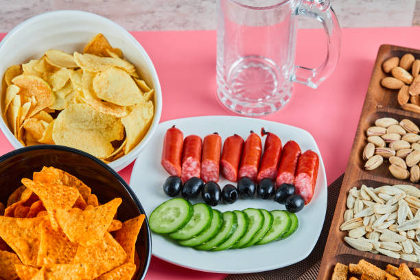 istock Assorted snacks on the pink table. Chips, sausages, pistachios, olives 1298518117