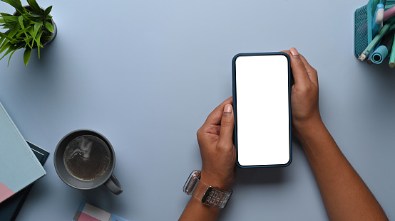 Overhead shot of man hands holding mock up smart phone on blue table. Blank screen for your text message or information content.