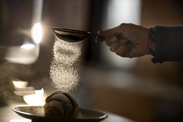 Sprinkling powdered sugar on croissant! Close up of unrecognizable woman sprinkling powdered sugar from a sieve on a croissant. sprinkling powdered sugar stock pictures, royalty-free photos & images