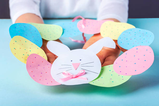 bricolage et créativité des enfants. instruction étape par étape: comment faire couronne de pâques en papier. étape11 mains d’enfants retenant la couronne mignonne finie des oeufs en papier et du lapin. artisanat de pâques fait main. - figurine easter egg easter holiday photos et images de collection