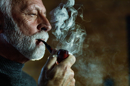 Serious senior man smoking a pipe. Copy space.