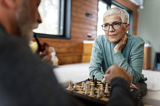 Senior woman waiting for her husband to make a move while playing chess at home.