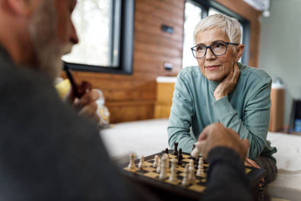 Relaxed mature couple playing chess at home. Senior woman waiting for her husband to make a move while playing chess at home. senior chess stock pictures, royalty-free photos & images