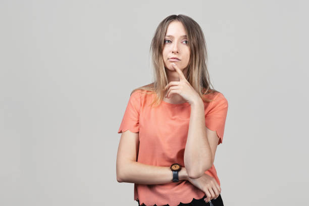 istock Pensive blond girl with thoughtful expression, keeps hand on chin, plans something or makes choice 1298525662
