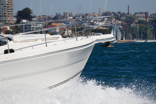 A motorboat speeding by in Sydney Harbor. Water splashes. Backdrop of Darling Point. View of the boat's bow