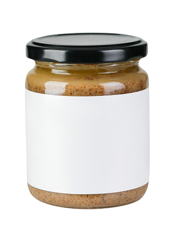 Glass jar full of peanut butter with black closed lid, white blank label