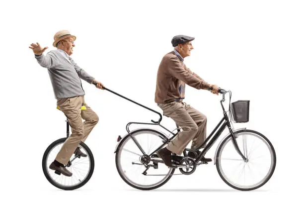 Elderly man riding a bicycle and pulling another man with a tricycle and walking cane isolated on white background