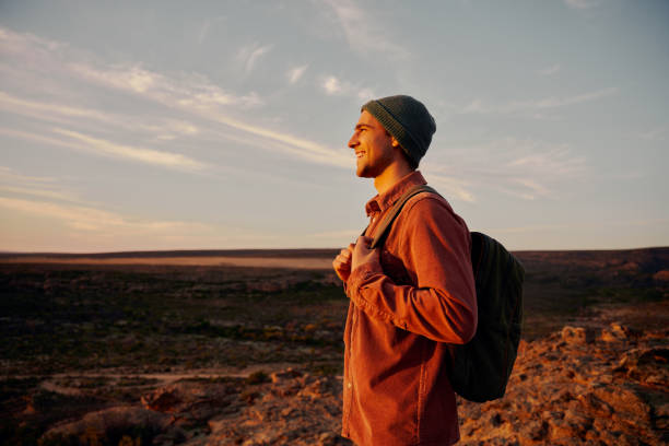 istock Happy hiker holding backpack looking at morning sunrise after successfully reaching mountain top 1298537136