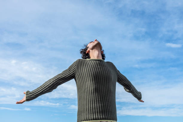 young man with open hands looking at the sky stock photo