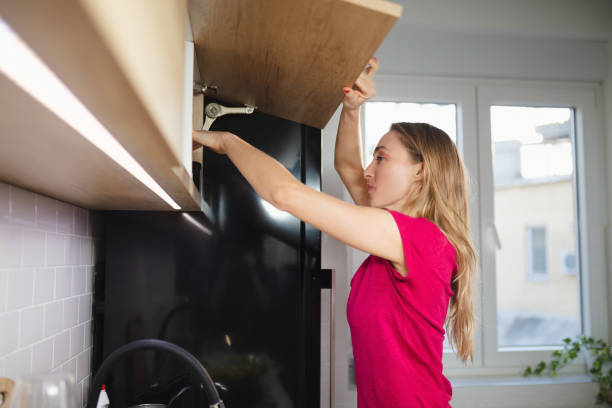 blonde woman opening upper kitchen cabinet and reaching in - upper arm fotos imagens e fotografias de stock