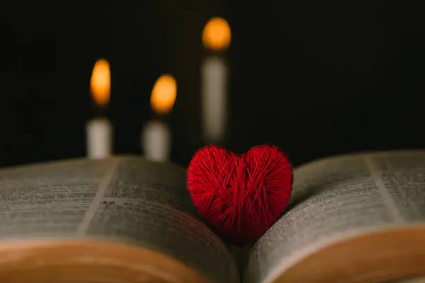 Photo of Education and Religion concept.Red heart and bible on a table by candlelight